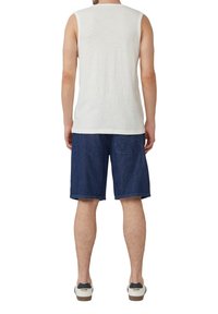 Witte mouwloze katoenen top gecombineerd met donkerblauwe denimshorts. De outfit heeft een relaxte fit en casual sneakers met een witte zool.
