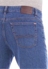 Jeans in denim blu con un'etichetta in pelle marrone, caratterizzati da una cucitura arancione a contrasto e un motivo di cucitura diagonale sulla tasca posteriore.