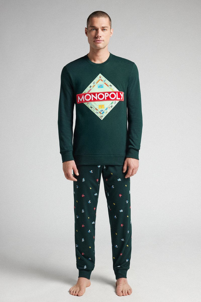Sudadera verde con el logo de "MONOPOLY", combinada con pantalones de pijama verde oscuro que presentan pequeños patrones coloridos relacionados con juegos. Tejido suave, ajuste relajado.