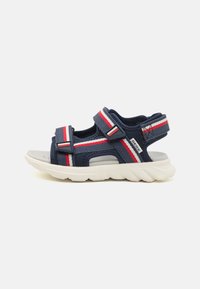 Navy blue athletic sandals with adjustable straps, red and white accents, breathable upper, and a thick, textured white sole.