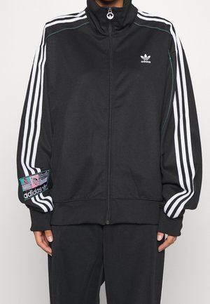 Chaqueta deportiva negra con cremallera completa, confeccionada en tela con rayas blancas a lo largo de las mangas y un parche con logo en colores llamativos en el brazo.