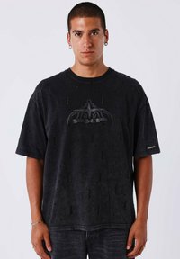 Zwart oversized T-shirt met een versleten textuur, ronde halslijn en een opvallende grafische print in het midden. Korte mouwen.