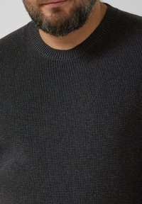 Ciemnoszary, dziany sweter o prążkowanej fakturze i okrągłym dekolcie. Widoczne detale przeszyć i lekko luźny krój.