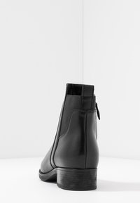 Bottines en cuir noir avec une finition lisse, des panneaux latéraux élastiques et un petit talon en bois. Détail de fermeture éclair à l'arrière pour un enfilage facile.