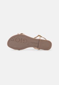 Sandale beige avec une semelle en caoutchouc texturée, dotée de fines lanières et d'une petite boucle. Logo embossé sur la semelle. Design plat, adapté à un usage décontracté.