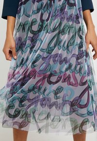 Vestido transparente y multicolor con patrones de escritura en espiral en verde azulado, púrpura y rosa. Tejido ligero con un diseño fluido y en capas.