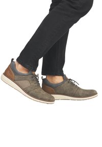 Chaussures pour hommes en daim vert olive, avec des accents gris et un talon en cuir marron. Elles sont dotées d'une semelle rembourrée et d'un design à lacets. Panneau latéral texturé.