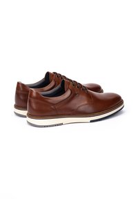 Par de zapatos de cuero marrón con cordones y suelas de goma blanca, mostrados uno al lado del otro sobre un fondo blanco.