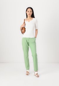 White short-sleeve top with scalloped hem, paired with light green pants. Accessories include a brown crossbody bag and white heeled sandals.
