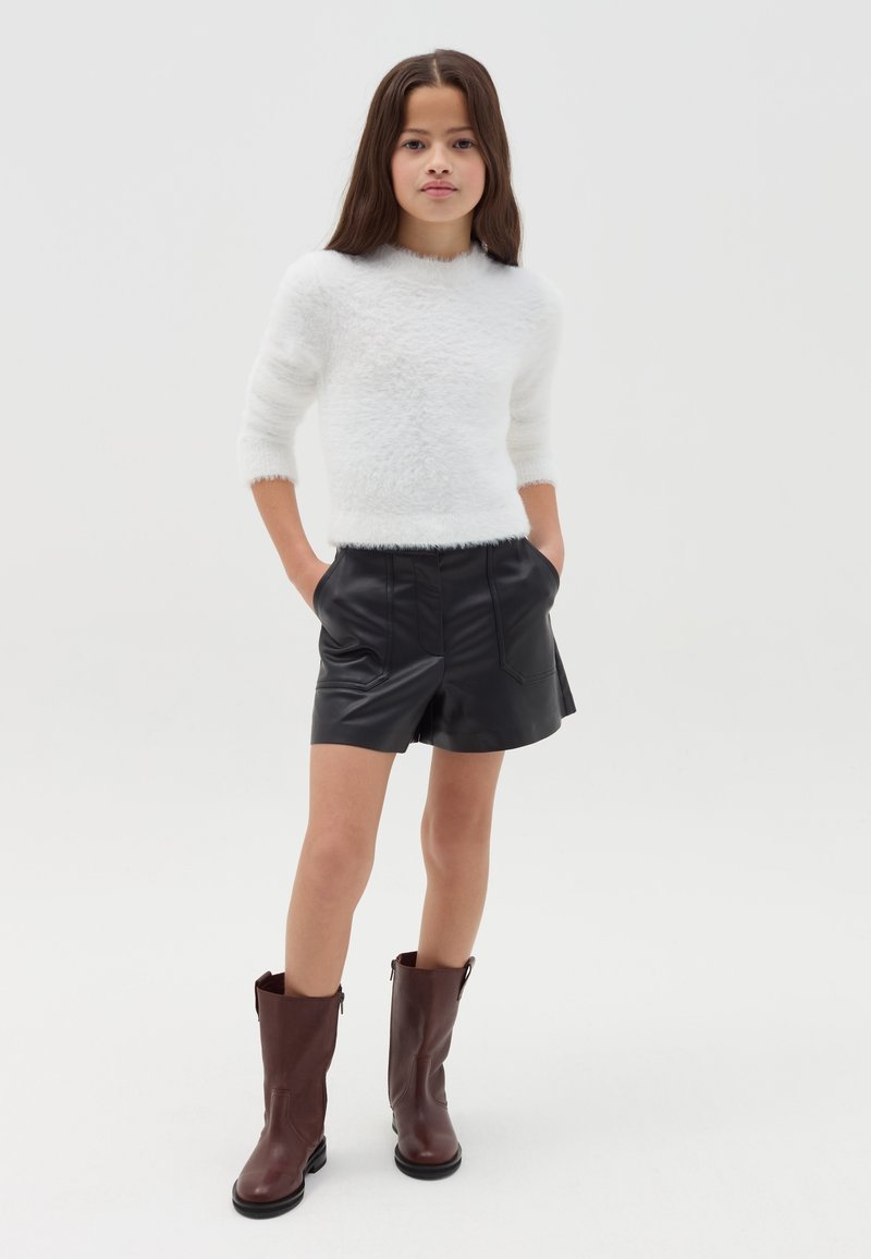 Maglione bianco in morbido peluche, pantaloni corti in pelle nera e stivali marroni al ginocchio. L'outfit presenta un design semplice con linee pulite e una texture liscia.