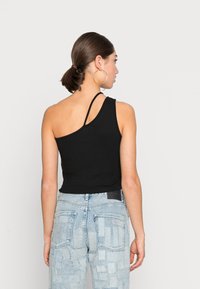 Top de algodão preto com um ombro só, com um formato ajustado. Combinado com jeans de denim de padrão azul claro, apresentando blocos quadrados e uma cintura alta.