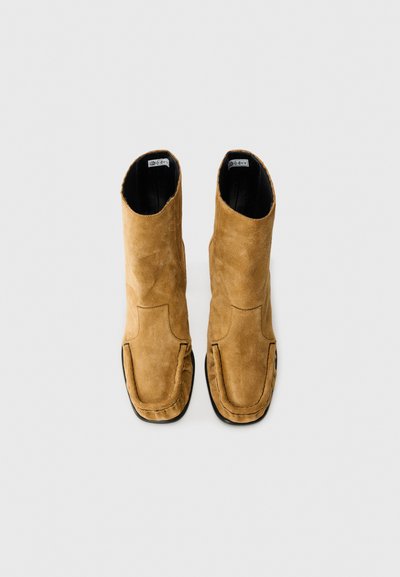 Bottines en suede beige avec une texture lisse, des orteils ronds et des détails de couture. L'intérieur est noir, sans matériel visible.