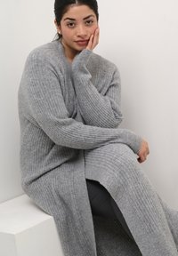 Lungo cardigan grigio a costine realizzato in morbido materiale a maglia, con scollatura aperta e spalle ribassate, maniche lunghe e spacchi laterali.