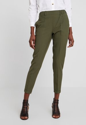 Pantalons taillés vert olive avec une taille ajustée, des jambes fuselées et un détail plissé à l'avant, associés à des sandales à talons noirs.