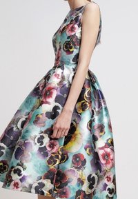 Vestido con estampado floral, con un torso ajustado y una falda acampanada. Presenta colores vibrantes, incluyendo púrpura, rojo y teal, sobre una tela similar al satén.