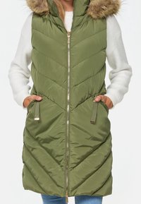 Groene gewatteerde vest met een chevronpatroon, rits aan de voorkant en een met bont gevoerde capuchon. Voorzien van zijzakken met gouden accenten en een middellange ontwerp.