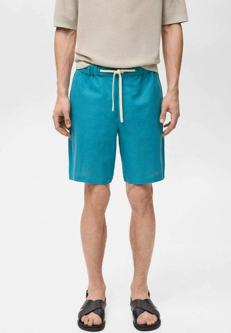 Pantaloni shorts turchesi realizzati in tessuto leggero, con una vita elasticizzata e un laccio beige, dal taglio rilassato, abbinati a sandali neri.