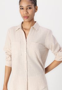 Light beige button-up shirt with a textured pattern, long sleeves rolled to elbows, and two chest pockets. Fabric appears soft and breathable.