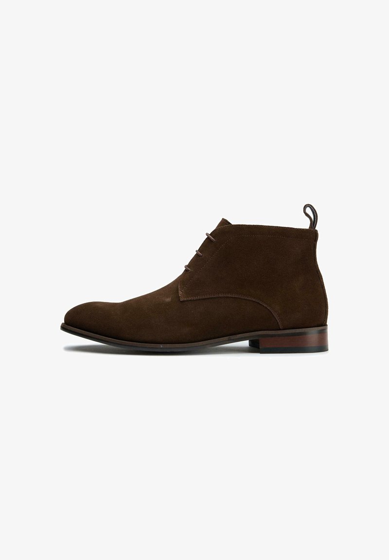 Brown suede ankle boots with a rounded toe, minimal stitching, and a small heel. Features a looped pull tab at the back.