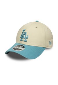 Gorra de béisbol color crema con visera azul claro, que presenta un logo bordado de "LA" en azul. Hecha de tela con un acabado texturizado.