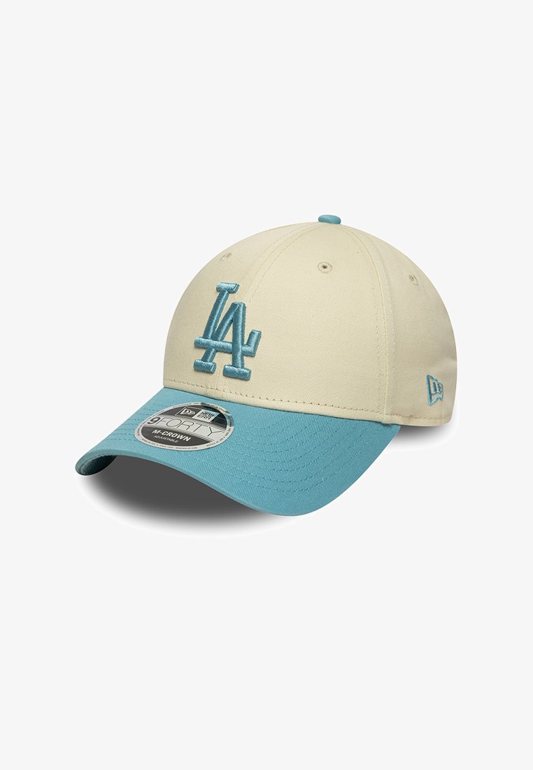 Gorra de béisbol color crema con visera azul claro, que presenta un logo bordado de "LA" en azul. Hecha de tela con un acabado texturizado.