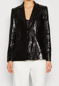 Černý kabát s flitry a klopovým límcem, uzavírání na jeden knoflík a dvě přední kapsy. Hladká textura s reflexním povrchem. Dlouhé rukávy.