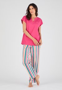 Haut rose à manches courtes avec un col henley, associé à un pantalon rayé multicolore avec des lignes verticales rouges, bleues et jaunes.