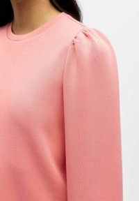 Lichtroze sweatshirt met een ronde halslijn en zachte poffende mouwen. De stof lijkt glad en heeft een licht rekbare textuur.