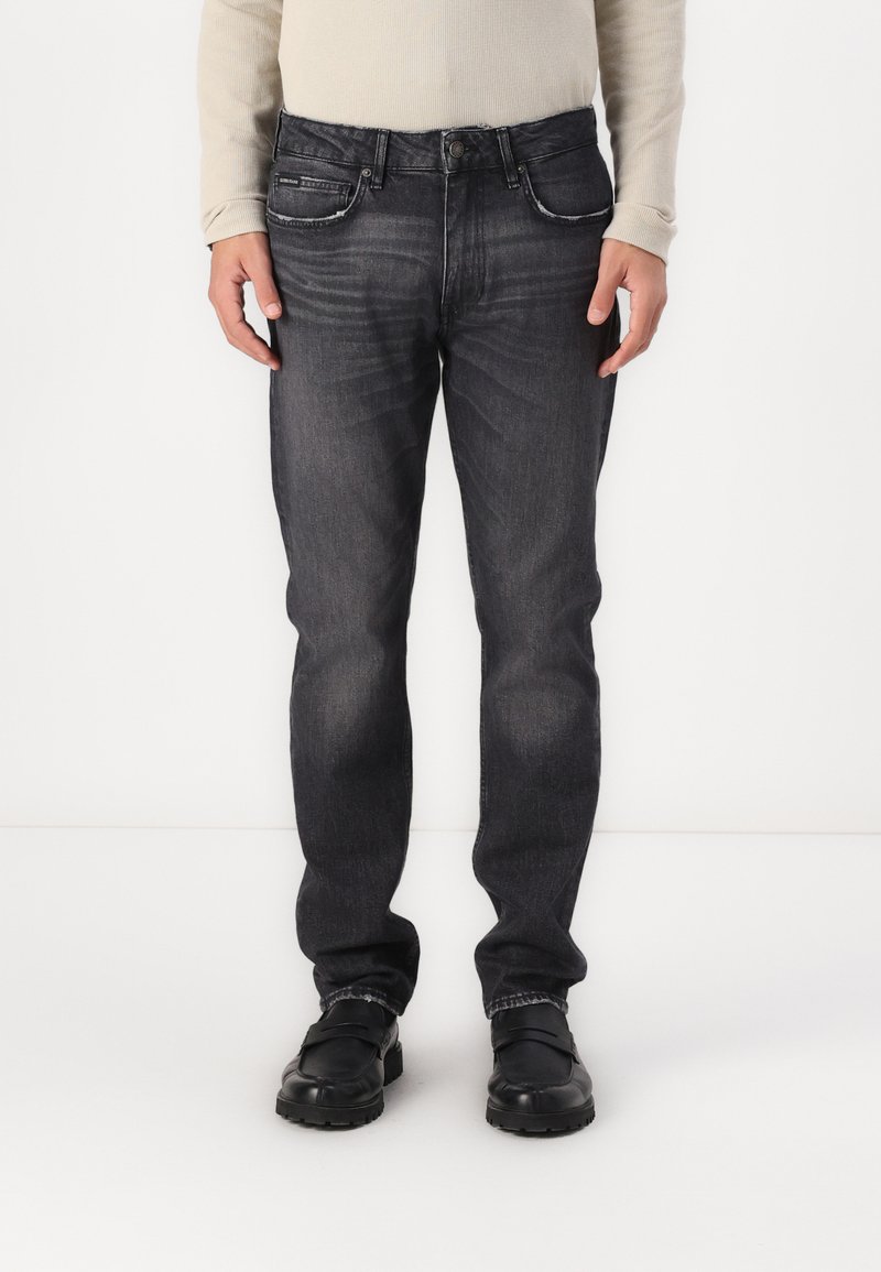 Temno pranje jeans hlače s straight leg dizajnom, pet žepov in neopaznim zbledeljem na stegen. Nosi se z črnimi čevlji.