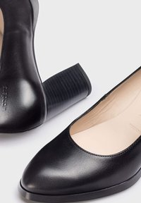 Zapatos de tacón alto de cuero negro con punta redonda, tacón cuadrado texturizado negro y acabado suave. El interior es de color claro.
