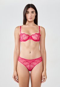 Reggiseno in pizzo rosa e slip coordinati, con un motivo a onde e dettagli trasparenti. Spalline regolabili, texture liscia.