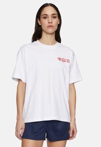 Valkoinen puuvillapaita, jossa on punaisella kirjailtu "R.S.V.P." -logo vasemmassa rinnassa. Irtonainen malli, pyöreä pääntie ja lyhyet hihat.