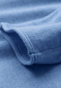 Tessuto morbido di un blu chiaro, con una superficie texturizzata, che presenta un bordo piegato e una delicata cucitura decorativa.