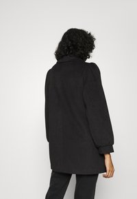 Abrigo negro con cuello camisero y mangas abullonadas, confeccionado en tela texturizada con una silueta recta y diseño hasta la rodilla.