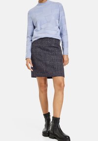 Lyseblå strikket sweater med teksturerede mønstre, parret med en mørk tweed nederdel. Sorte chunky hælankel støvler fuldender outfittet.