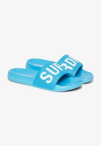 Blauwe schuifsandalen met een brede band waarop het woord "SUPERDRY" in dikke witte letters staat. Soepele textuur en afgeronde vorm.