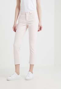 Vaqueros de denim rosa claro con corte ajustado, longitud recortada, cinco bolsillos y cierre de botón, combinados con zapatillas blancas.
