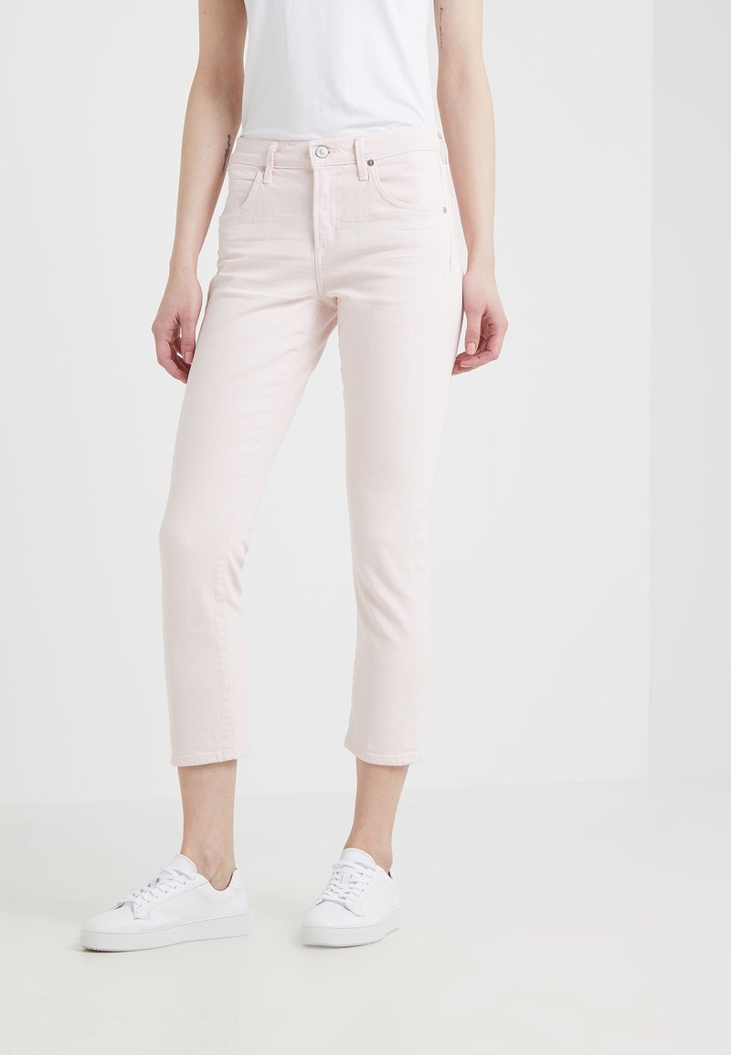 Vaqueros de denim rosa claro con corte ajustado, longitud recortada, cinco bolsillos y cierre de botón, combinados con zapatillas blancas.