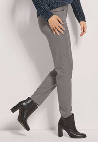 Grijze slim-fit broek gecombineerd met zwarte enkellaarsjes met hak. De laarsjes hebben een gladde ledertextuur en een stevige blokhak.