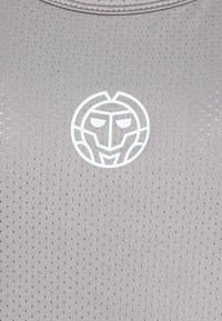 Šedá texturovaná látka s opakovaným perforovaným vzorem; bílé grafické logo připomínající stylizovanou tvář je umístěno ve středu.