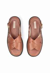 Sandales en cuir marron avec design à lanières croisées, bride arrière réglable et semelle en caoutchouc noir texturée. Finition lisse avec surpiqûres contrastées.