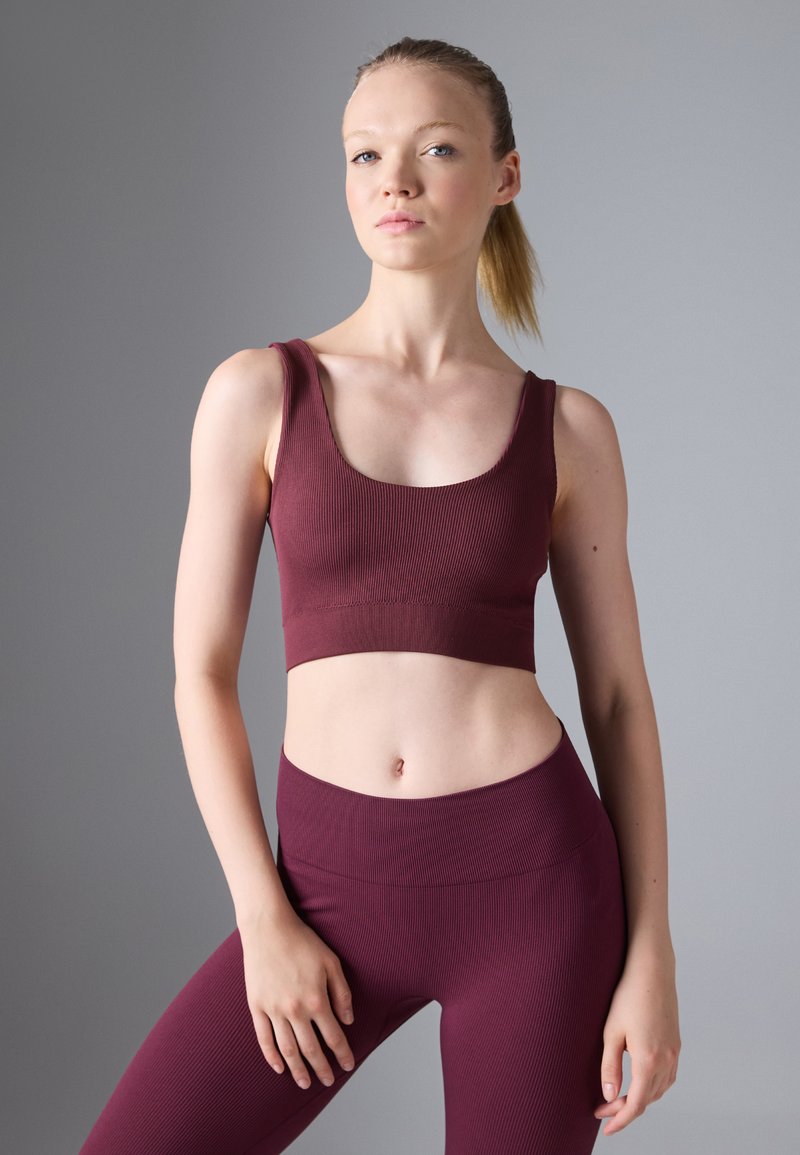 Top deportivo corto de color marrón oscuro con textura acanalada y tirantes anchos, combinado con leggings de cintura alta a juego. Diseño liso y ajustado.