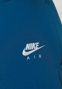 Nike Air-Produkt aus dunkelblauem Stoff mit glatter Textur und reflektierendem silbernem Logo. Das Design umfasst eine stromlinienförmige Form und einen minimalistischen Stil.