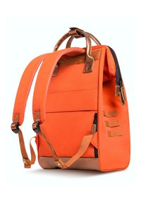 Sac à dos en tissu orange avec des accents marron, des bretelles rembourrées, plusieurs poches et une poignée supérieure. Présente un design structuré et angulaire.