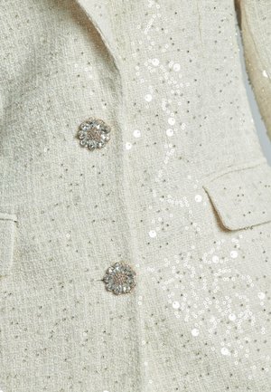 White tweed jacket with sequin embellishments, featuring a textured fabric and floral crystal buttons, double-breasted design with pockets.