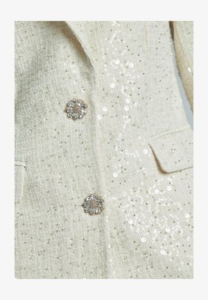 Giacca bianca in tweed con decorazioni in paillettes, caratterizzata da un tessuto testurizzato e bottoni in cristallo a forma di fiore, design doppiopetto con tasche.