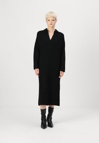 Must have mustribliline kudumkleit V-kaeluse ja pikkade varrukatega. Omab külgnihkeid ja vabalt langetatud lõiget. Kombineeritud põlvikute kõrguste mustade saapadega.