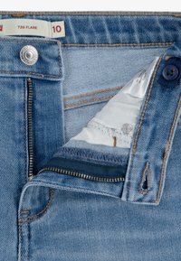 Jasnoniebieskie dżinsy z zamkiem częściowo otwartym, z zapięciem na metalowy guzik oraz wewnętrzną metką rozmiaru, na której widnieje "726 FLARE" i rozmiar 10.