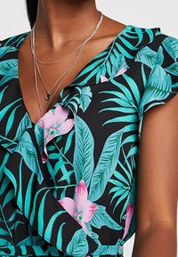 Bloemen wikkeljurk met een zwarte achtergrond, versierd met grote roze bloemen en teal bladeren. Zachte stof met gerimpelde mouwen en gelaagd ontwerp.