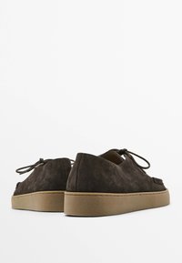 Brown suede shoes with a low profile, round toe, and lace-up design. Rubber soles and smooth texture with subtle stitching details.